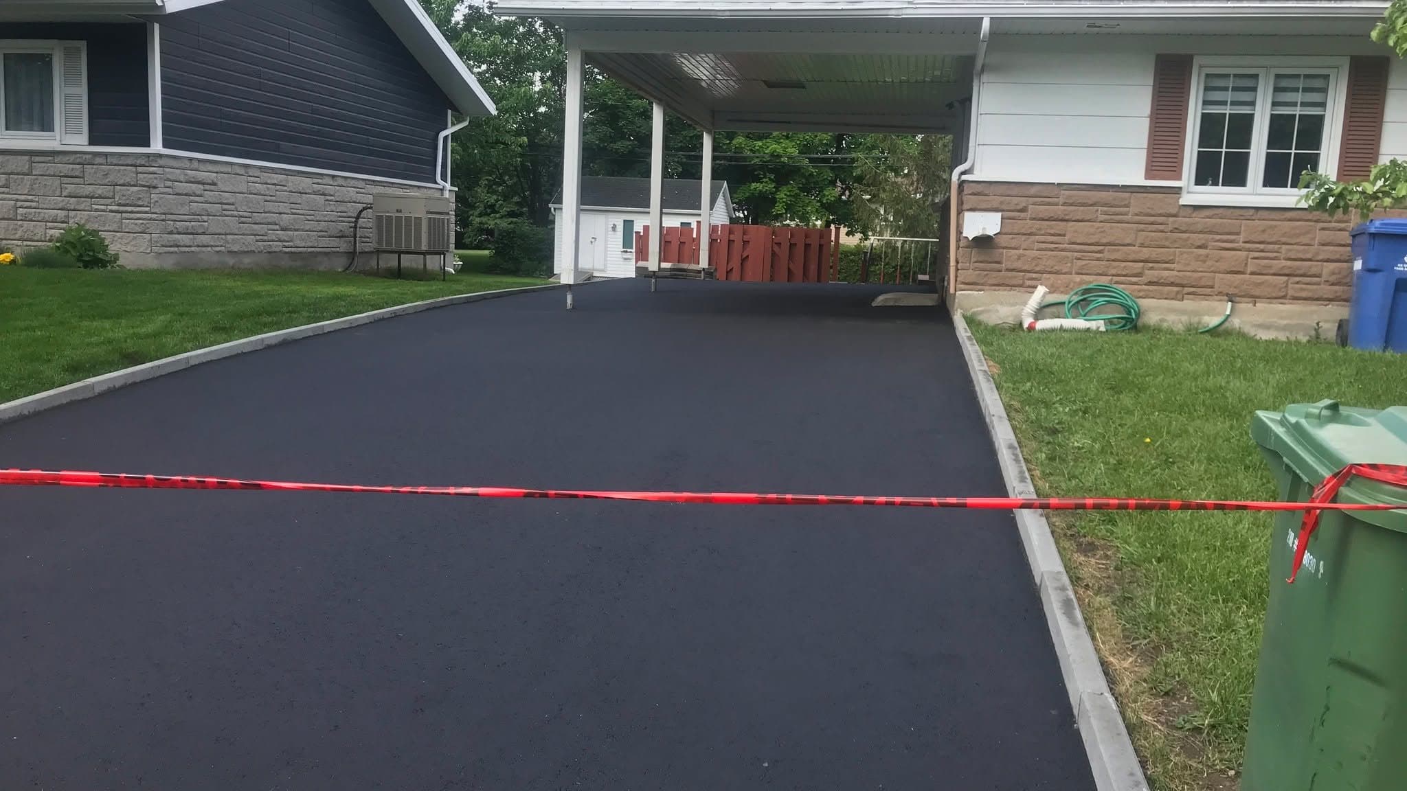 Entrée d'asphalte neuve devant un carport, ruban de chantier encore en place — chantier PAVEX terminé